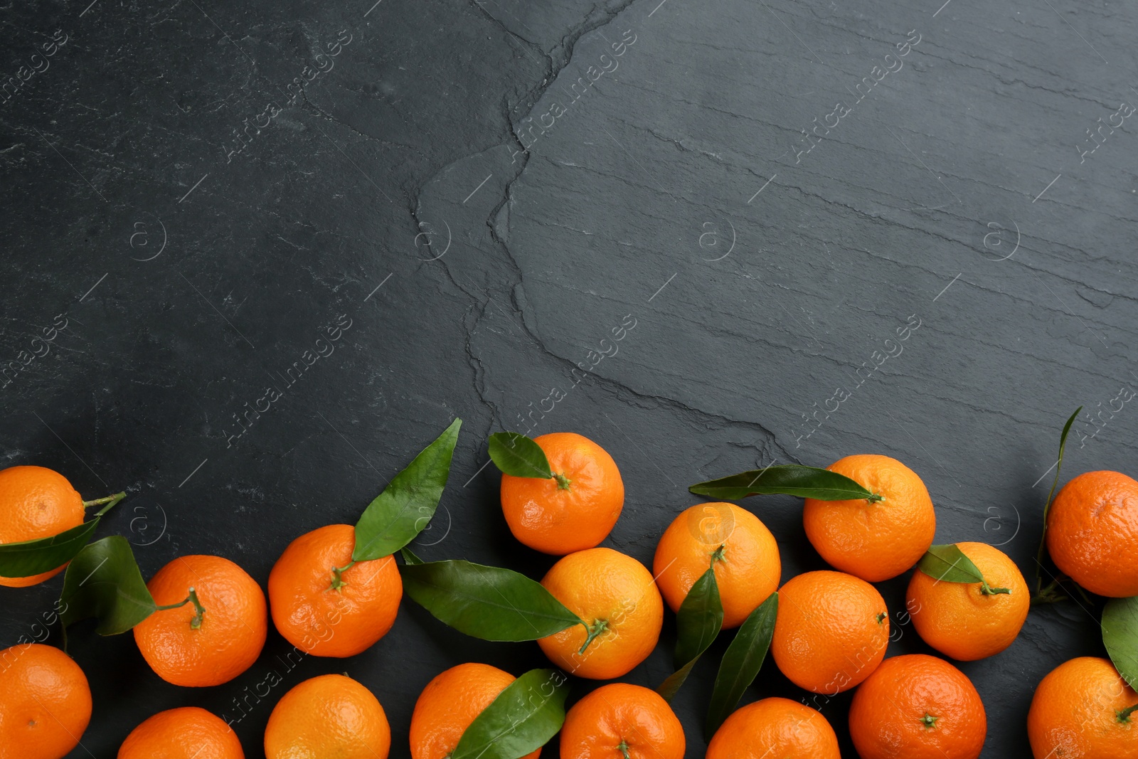 Photo of Fresh tangerines with green leaves on black table, flat lay. Space for text