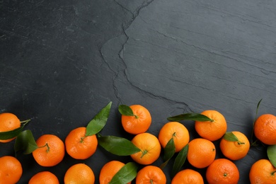 Fresh tangerines with green leaves on black table, flat lay. Space for text