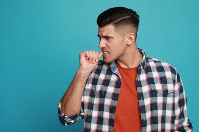 Photo of Man biting his nails on light blue background, space for text. Bad habit