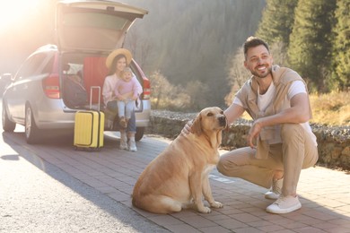 Photo of Happy man with dog, mother and her daughter sitting in car trunk outdoors. Family traveling with pet