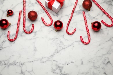 Photo of Tasty candy canes, Christmas balls and gift box on white marble table, flat lay. Space for text