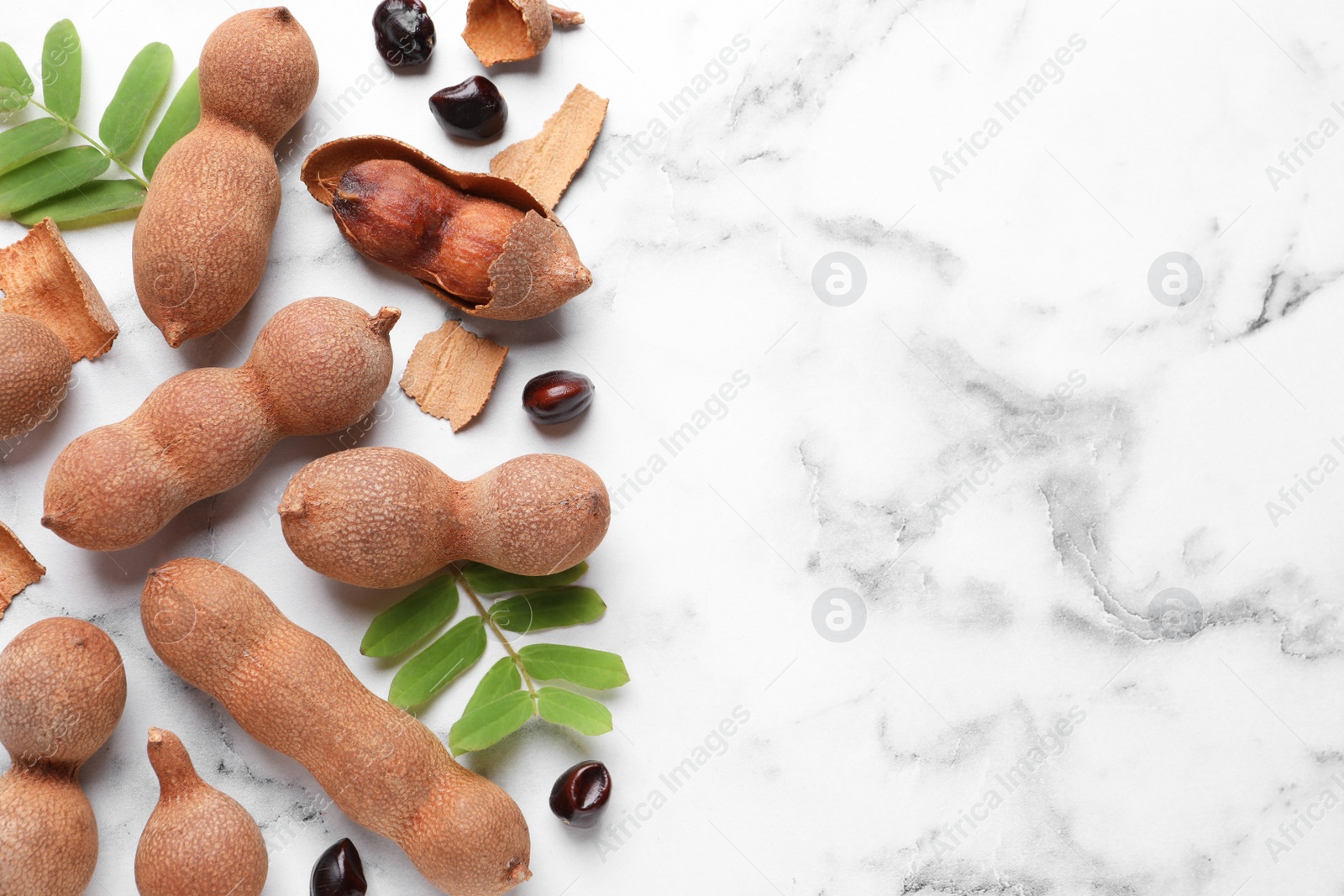 Photo of Ripe tamarinds and fresh leaves on white marble table, flat lay. Space for text