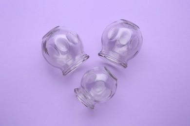 Photo of Glass cups on violet background, flat lay. Cupping therapy