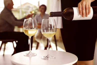 Waitress pouring wine into glass in restaurant, closeup