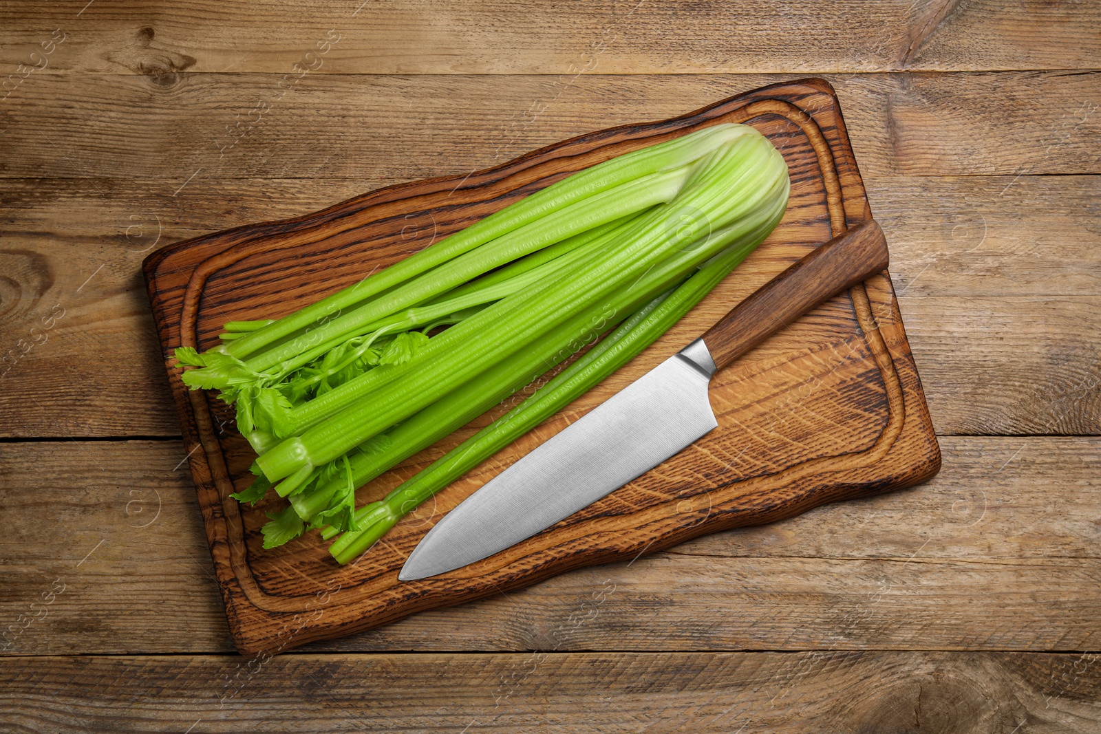 Photo of Fresh green celery and knife on wooden table, top view