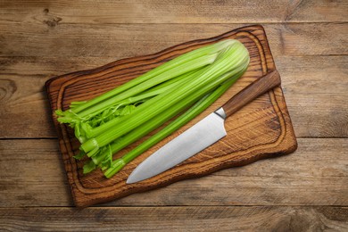 Fresh green celery and knife on wooden table, top view
