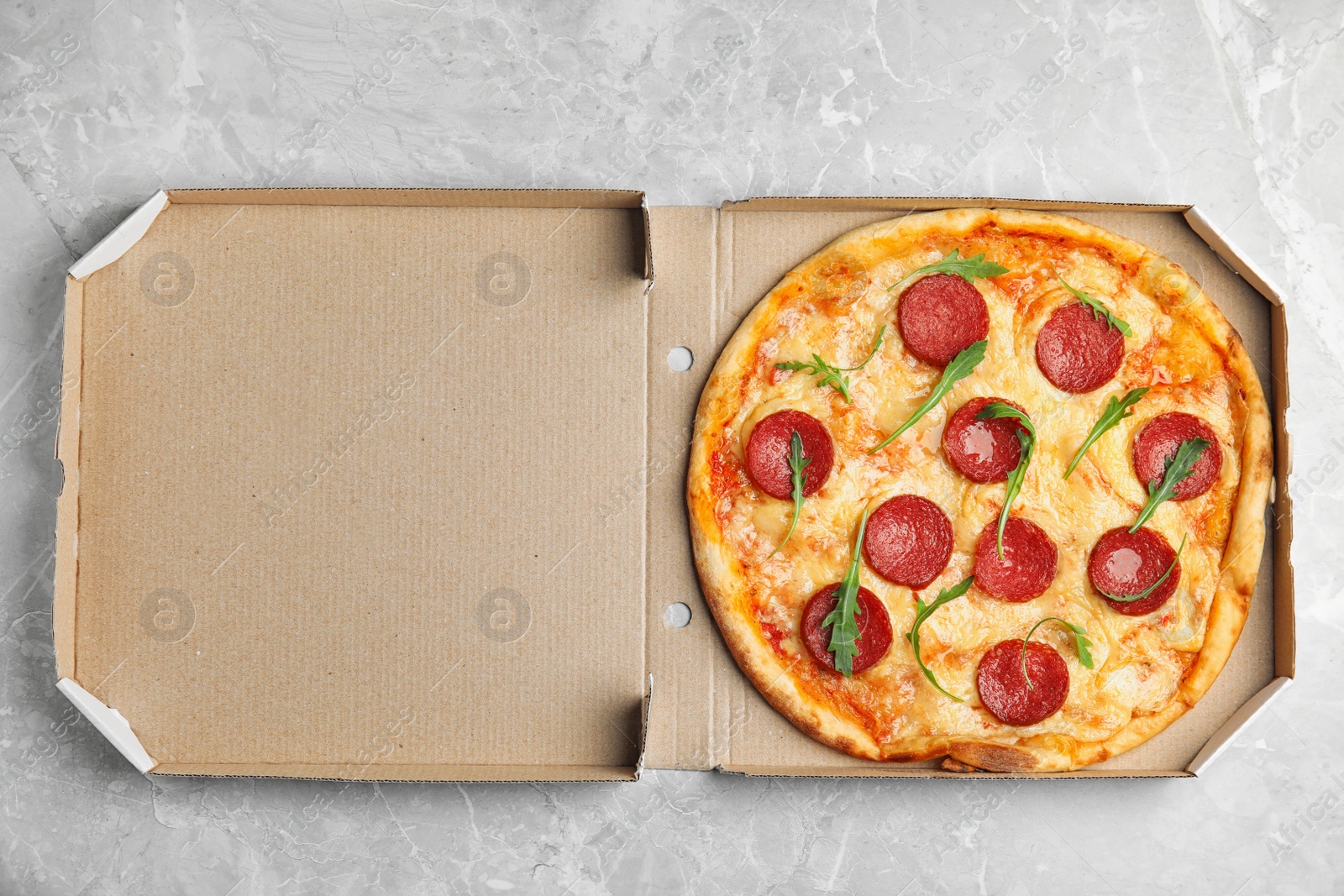 Photo of Tasty pepperoni pizza in cardboard box on light grey marble table, top view