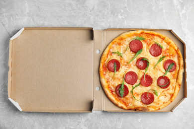 Photo of Tasty pepperoni pizza in cardboard box on light grey marble table, top view