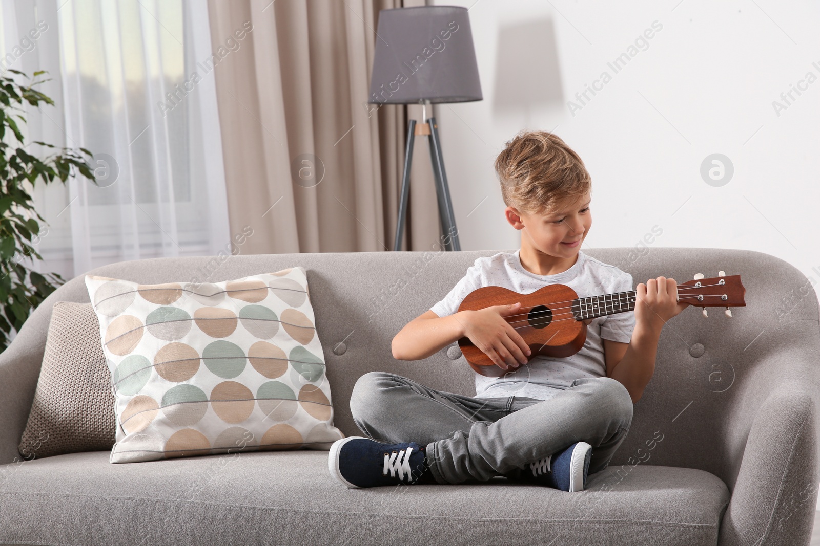 Photo of Little boy playing guitar on sofa in room. Space for text