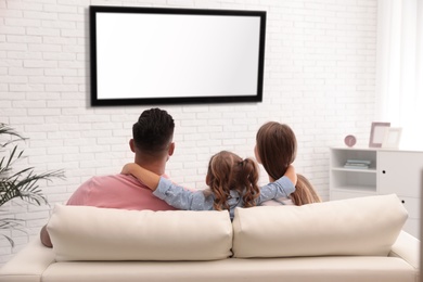 Photo of Family watching TV on sofa at home, back view