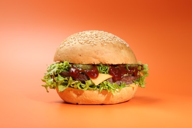 Photo of Delicious cheeseburger with lettuce, pickle, ketchup and patty on coral background, closeup