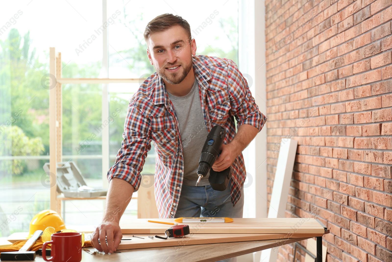 Photo of Young man working with electric screwdriver near brick wall