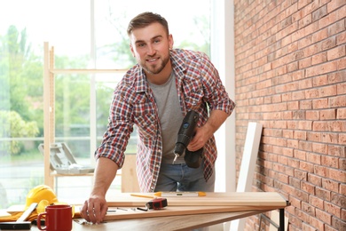 Photo of Young man working with electric screwdriver near brick wall