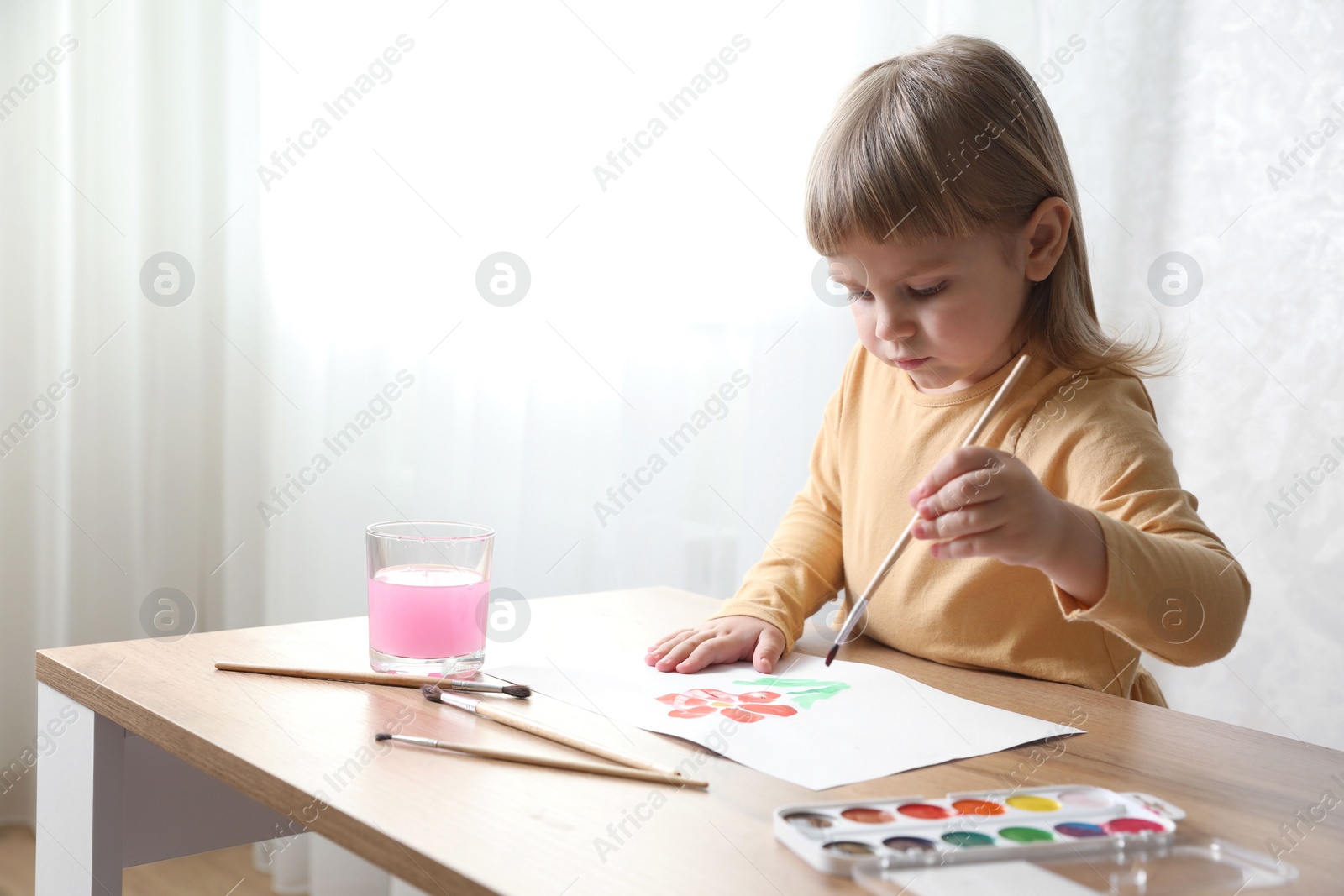 Photo of Cute little girl drawing with brush at wooden table indoors. Child`s art