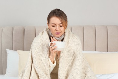 Sick woman with warm plaid and cup of drink in bed at home