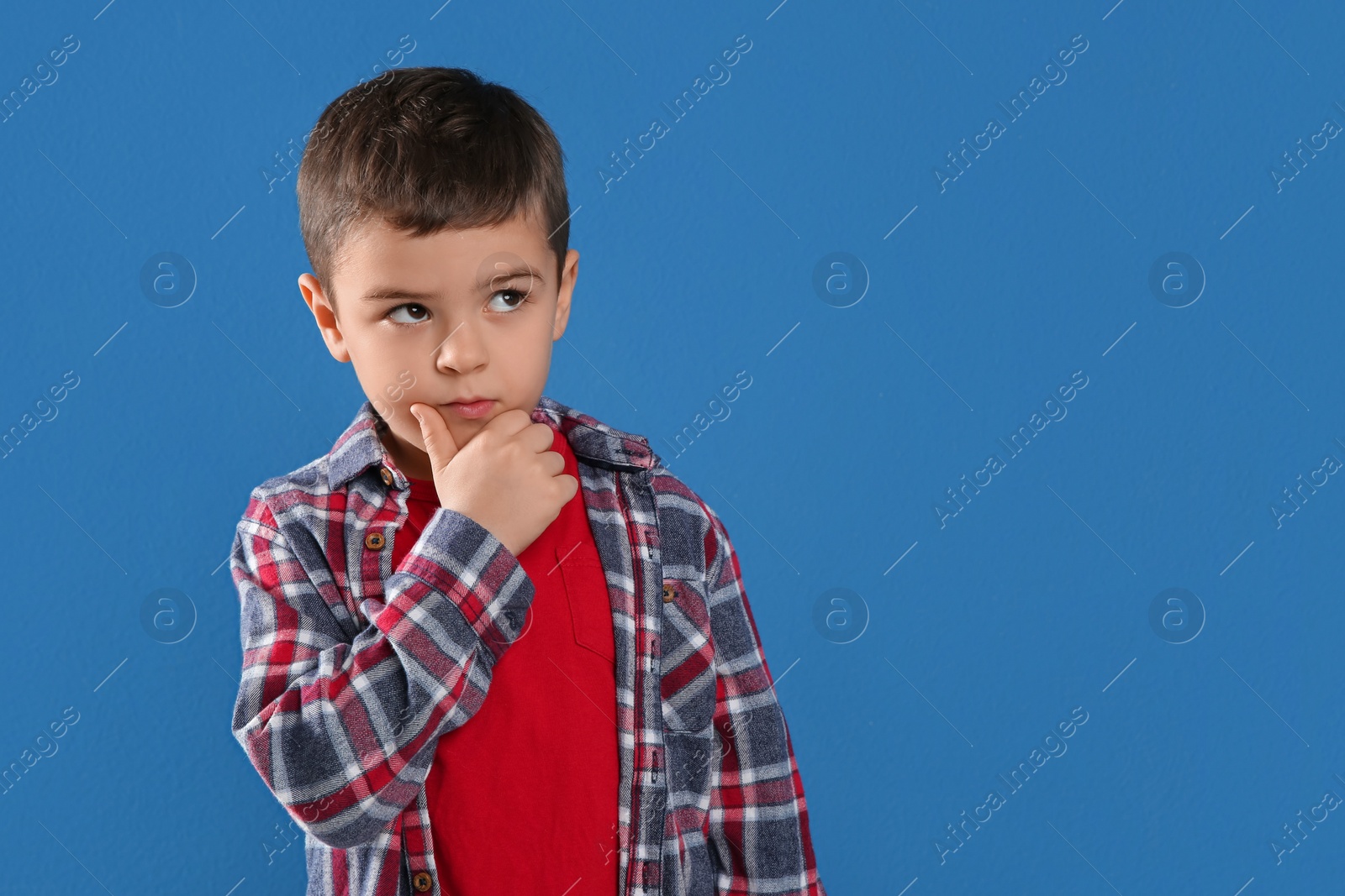 Photo of Thoughtful little boy on blue background, space for text