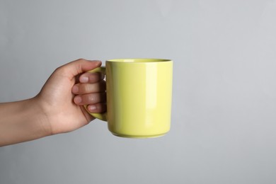 Photo of Woman holding yellow mug on light grey background, closeup