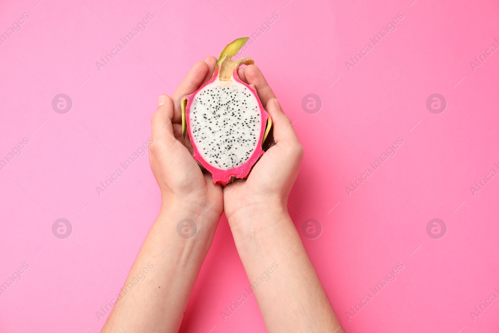 Photo of Woman holding half of delicious ripe dragon fruit (pitahaya) on pink background