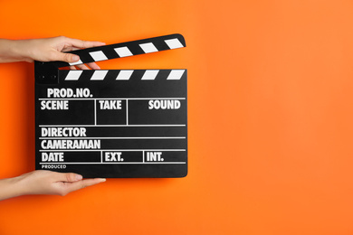 Woman holding clapperboard on orange background, closeup with space for text. Cinema production