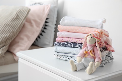 Photo of Toy bunny and stack of stylish child clothes on table indoors