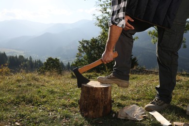 Photo of Man with axe cutting firewood in mountains, closeup