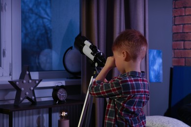 Photo of Little boy looking at stars through telescope in room, back view