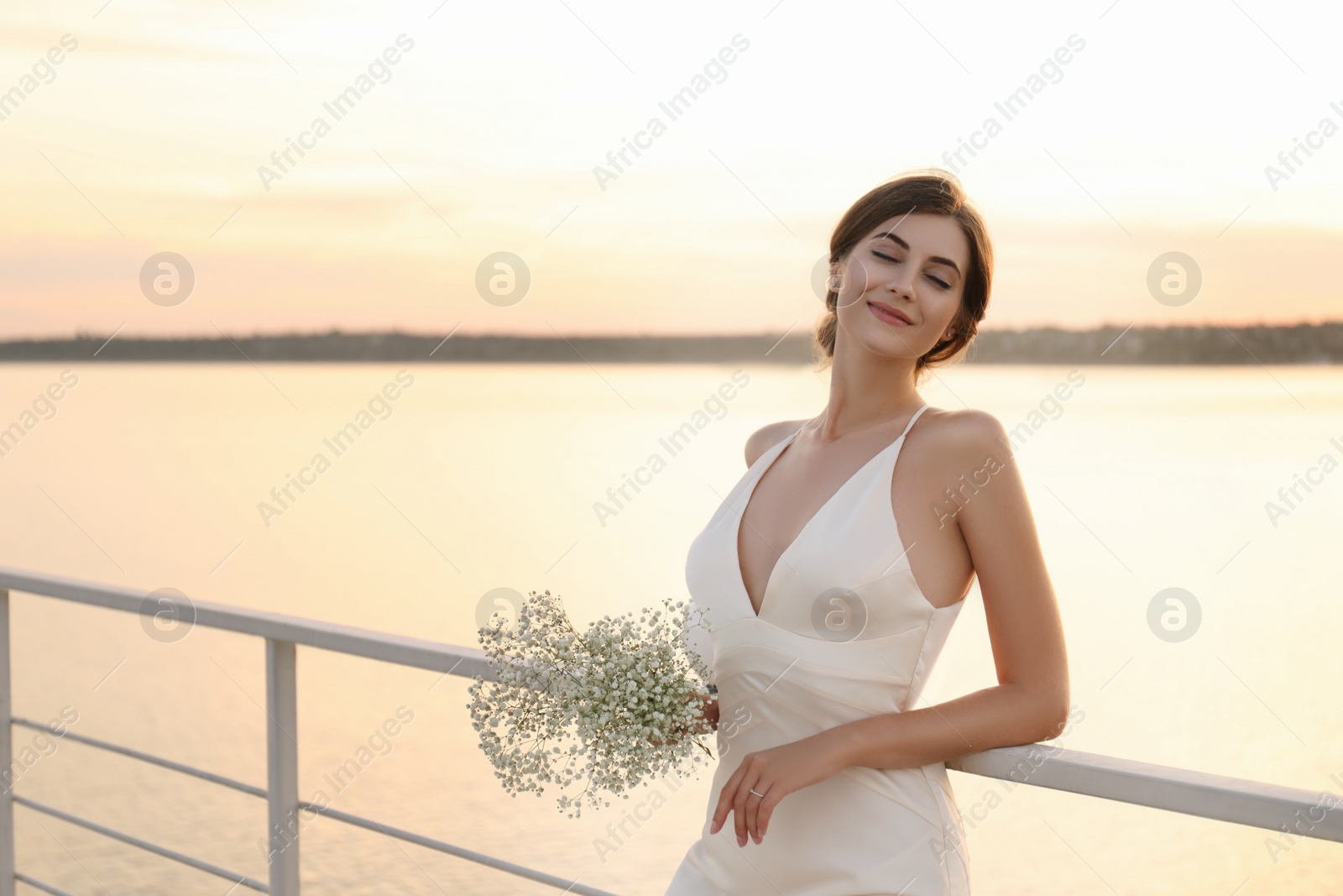 Photo of Gorgeous bride in beautiful wedding dress with bouquet near river on sunset