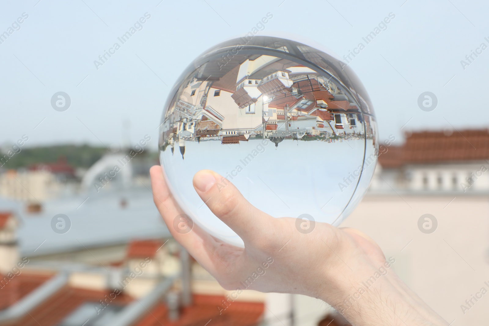 Photo of View of beautiful city street, overturned reflection. Man holding crystal ball outdoors, closeup