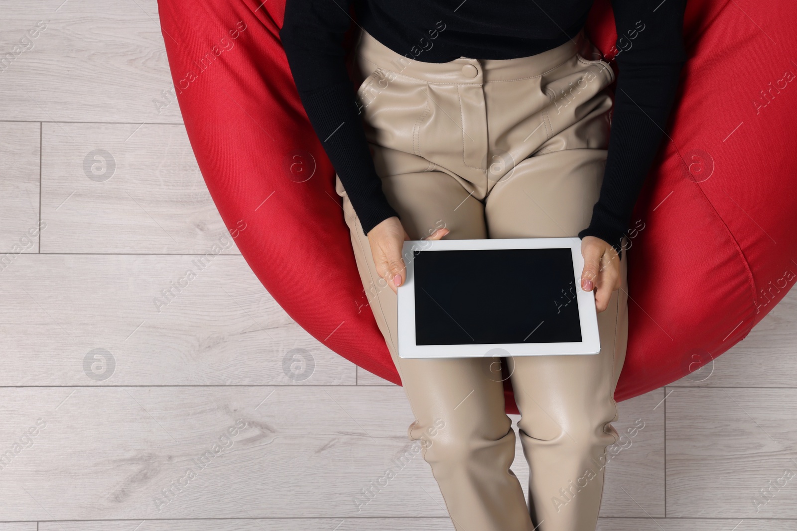 Photo of Woman working with tablet on beanbag chair, top view. Space for text