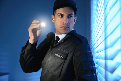 Photo of Professional security guard with flashlight near window in dark room