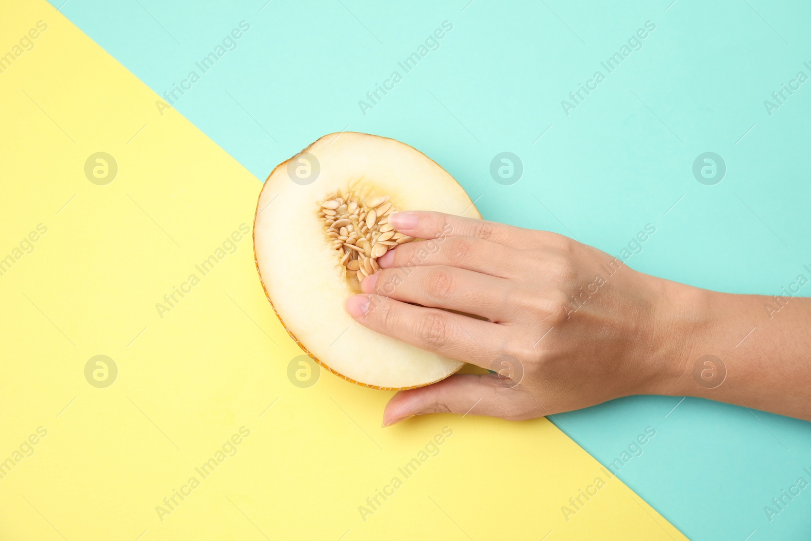 Photo of Young woman touching half of melon on color background, top view. Sex concept