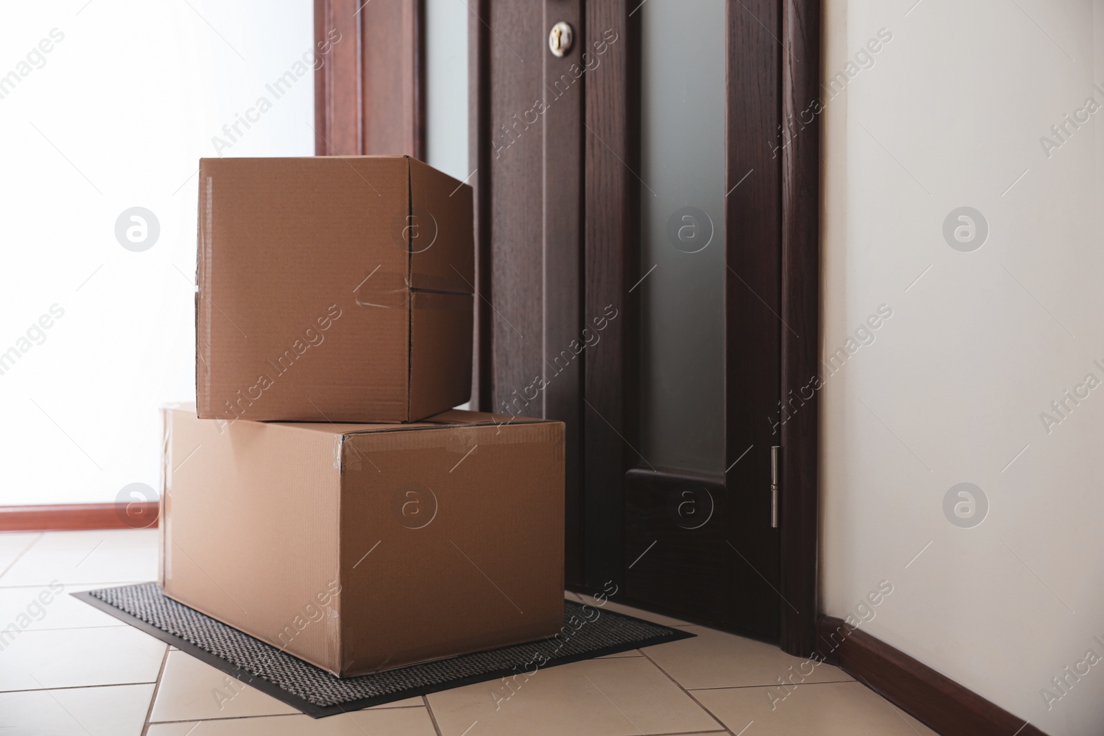 Photo of Cardboard boxes on rug near door. Parcel delivery service