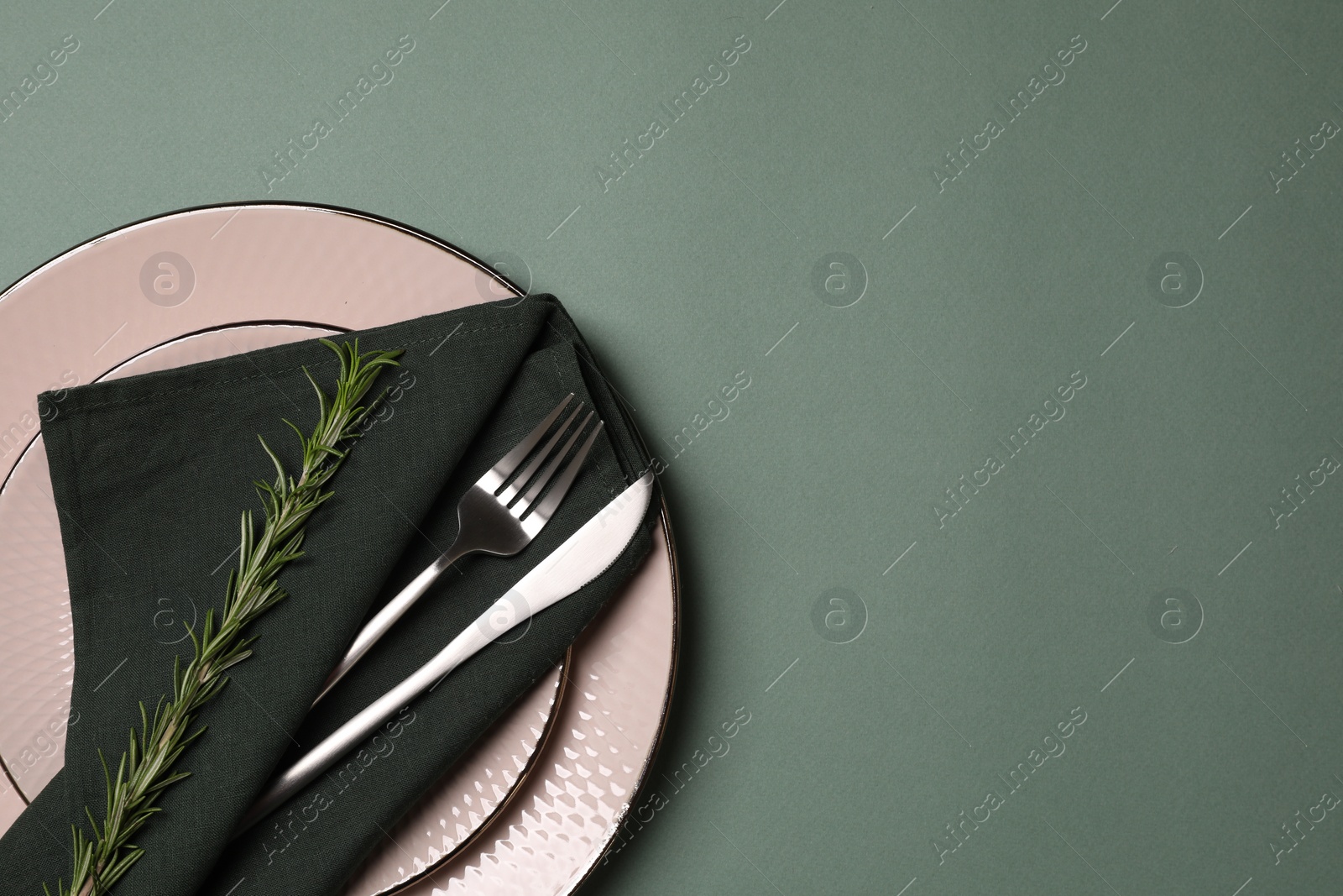 Photo of Stylish table setting. Plates, cutlery, napkin and rosemary on green background, top view with space for text