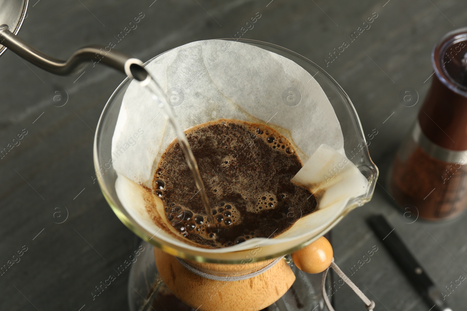 Photo of Pouring hot water into glass chemex coffeemaker with paper filter and coffee on gray table, above view