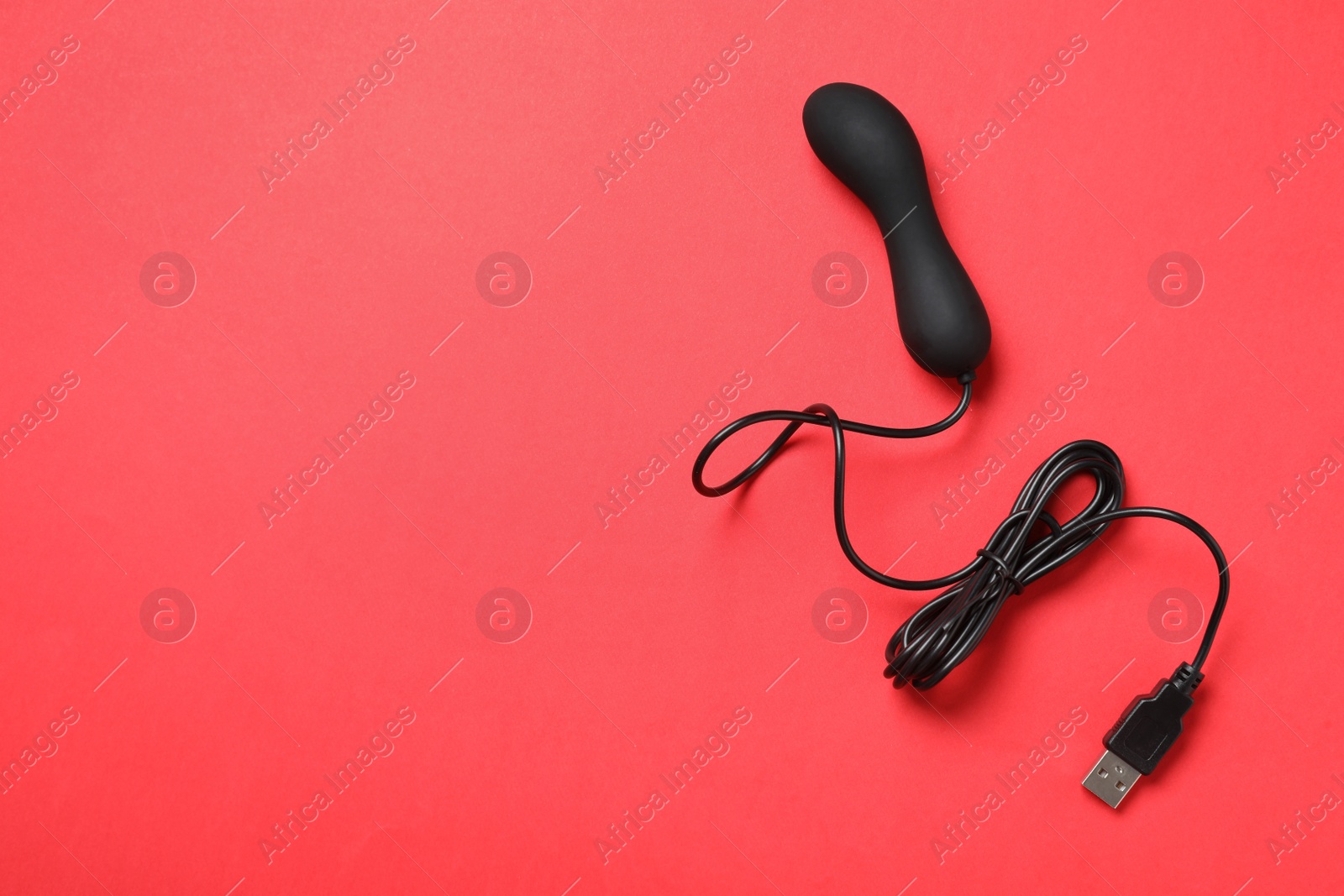 Photo of Black electric powered vibrator on red background, top view with space for text. Sex toy