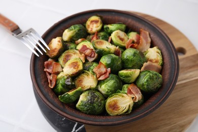 Photo of Delicious roasted Brussels sprouts and bacon in bowl on white table, closeup