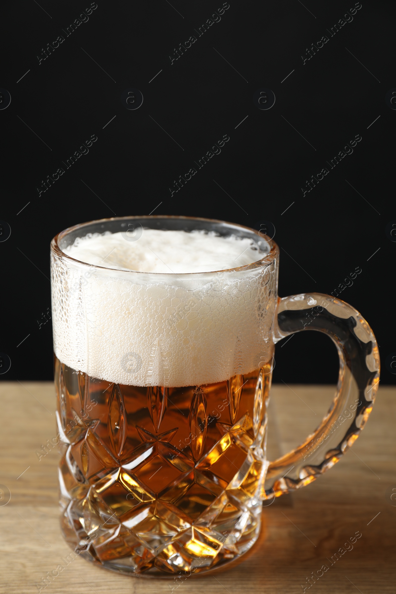 Photo of Mug with fresh beer on wooden table against black background