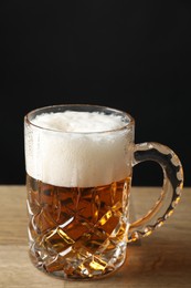 Mug with fresh beer on wooden table against black background