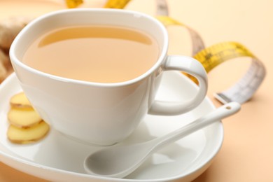 Cup of diet herbal tea and sliced ginger on orange background, closeup