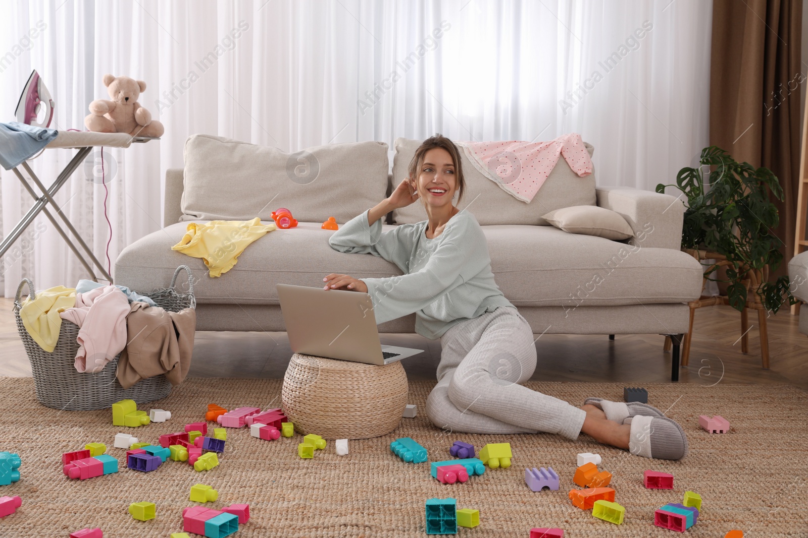 Photo of Young mother working with laptop on floor in messy room