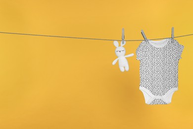 Baby onesie and bunny toy drying on laundry line against orange background, space for text