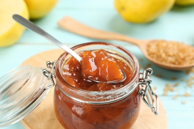 Photo of Delicious quince jam with spoon on light blue table, closeup