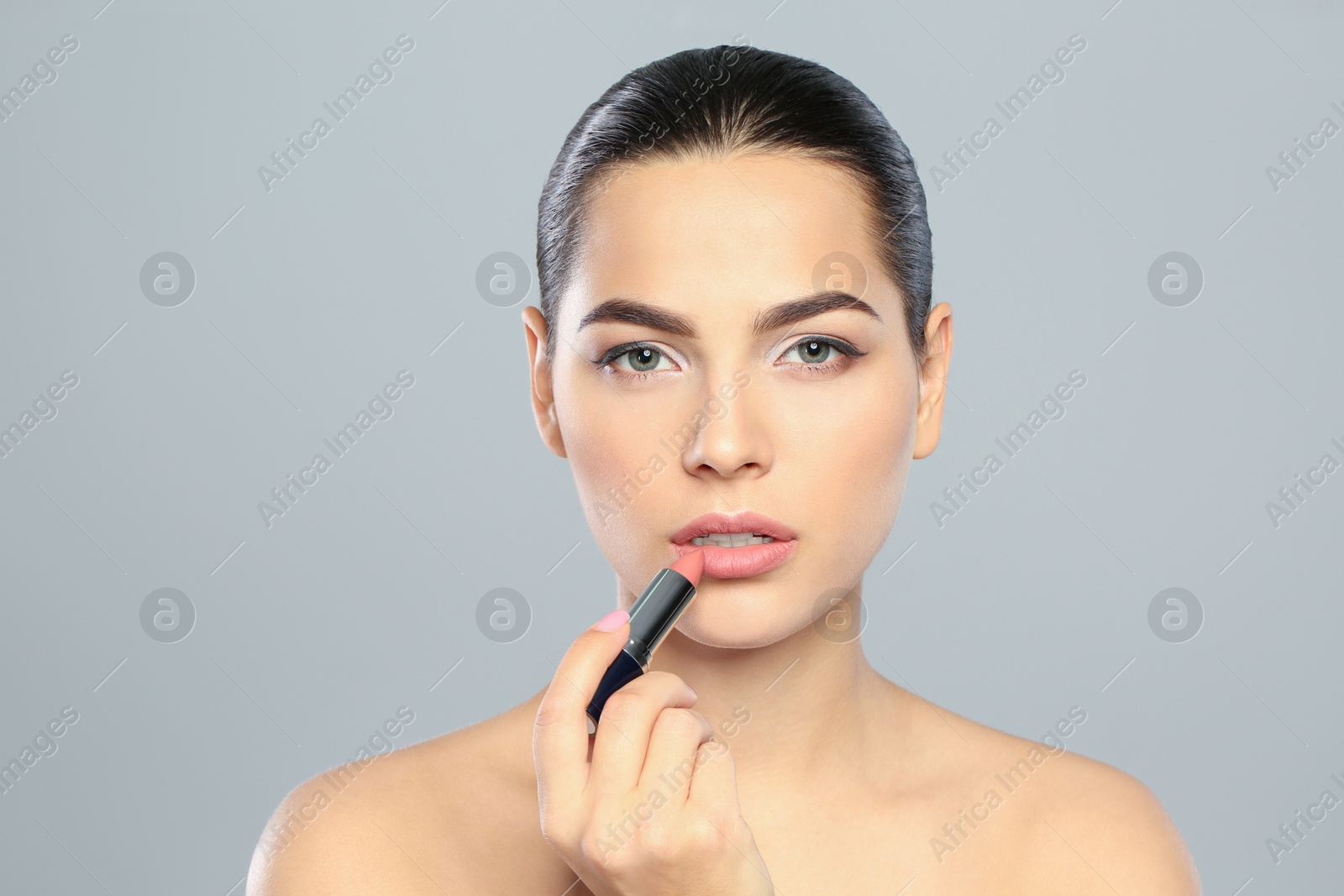 Photo of Young woman applying lipstick on color background