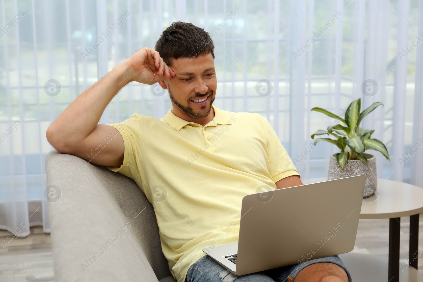 Photo of Happy man using laptop on sofa at home. Internet shopping