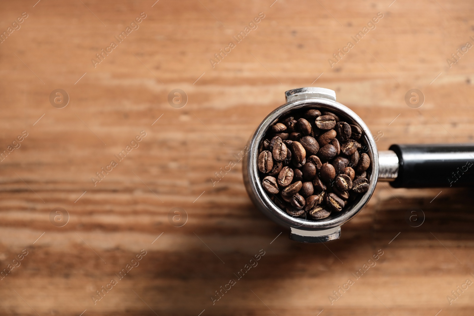 Photo of Portafilter with roasted coffee beans on wooden table, top view. Space for text