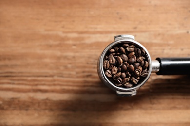 Portafilter with roasted coffee beans on wooden table, top view. Space for text