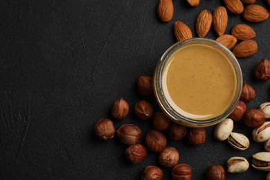 Photo of Delicious hazelnut butter and different nuts on black table, flat lay. Space for text