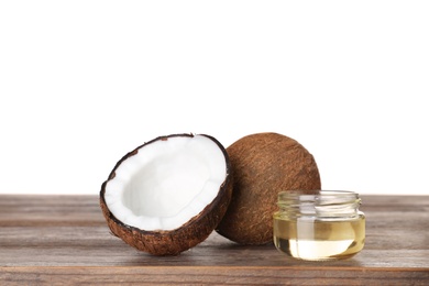 Photo of Coconuts and jar of natural organic oil on wooden table against white background