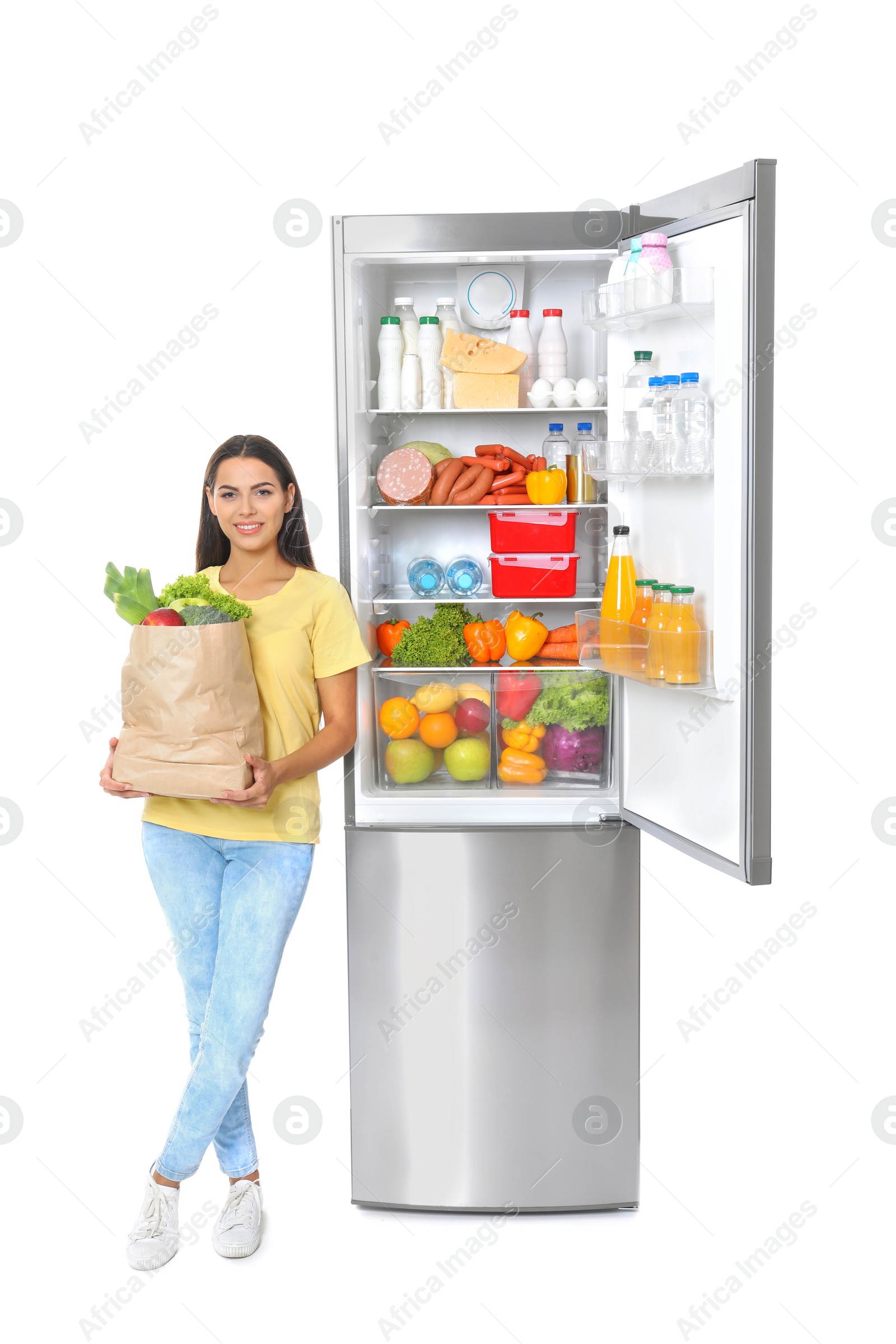 Photo of Young woman with bag of groceries near open refrigerator on white background