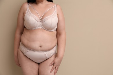 Beautiful overweight woman in underwear on beige background, closeup with space for text. Plus-size model